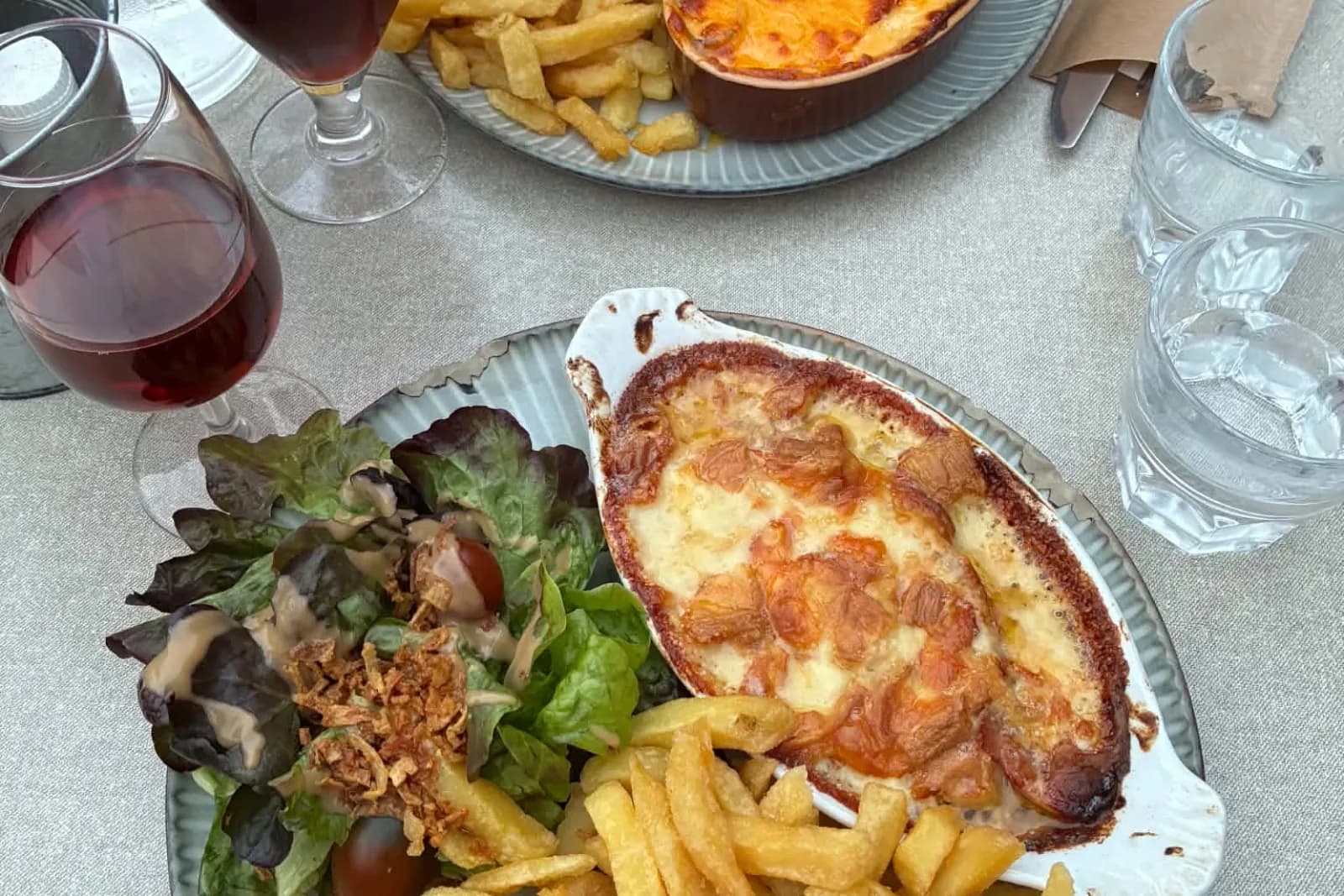 Deux gratins servis en cassolette avec des frites fraîches et une salade, devant deux bières.