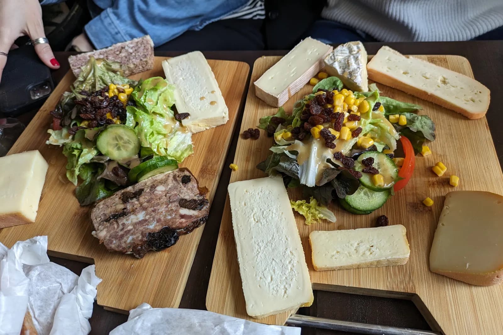 Deux planches de bois garnies de fromages du Nord, de pâté et de salade, posées sur une table.